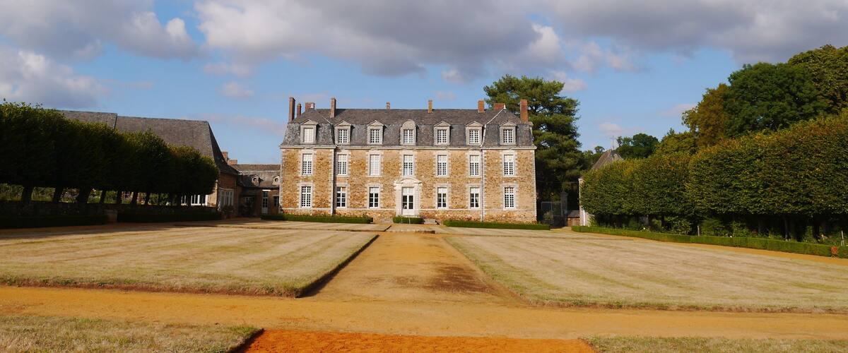 A large stone building with a symmetrical facade, surrounded by a well-maintained lawn and hedges.