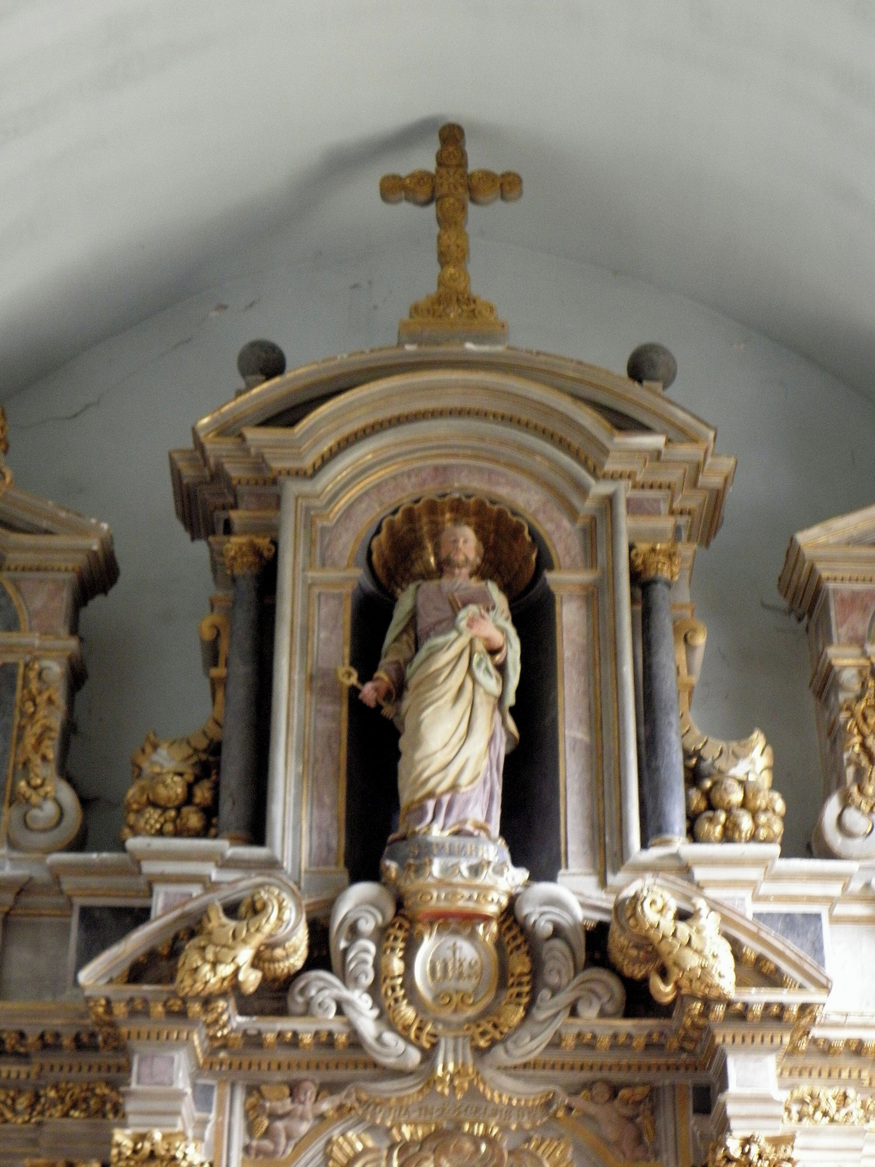 A statue of a robed figure with a cross above, surrounded by ornate gold and white architectural details.