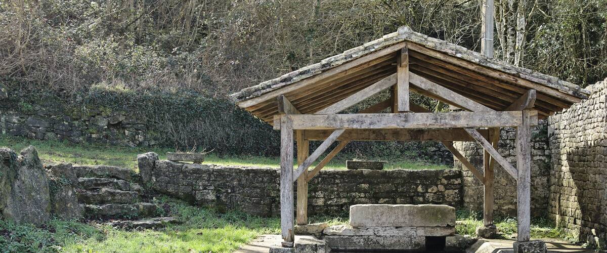 A stone structure with a wooden roof near a pond with clear water and rocks.