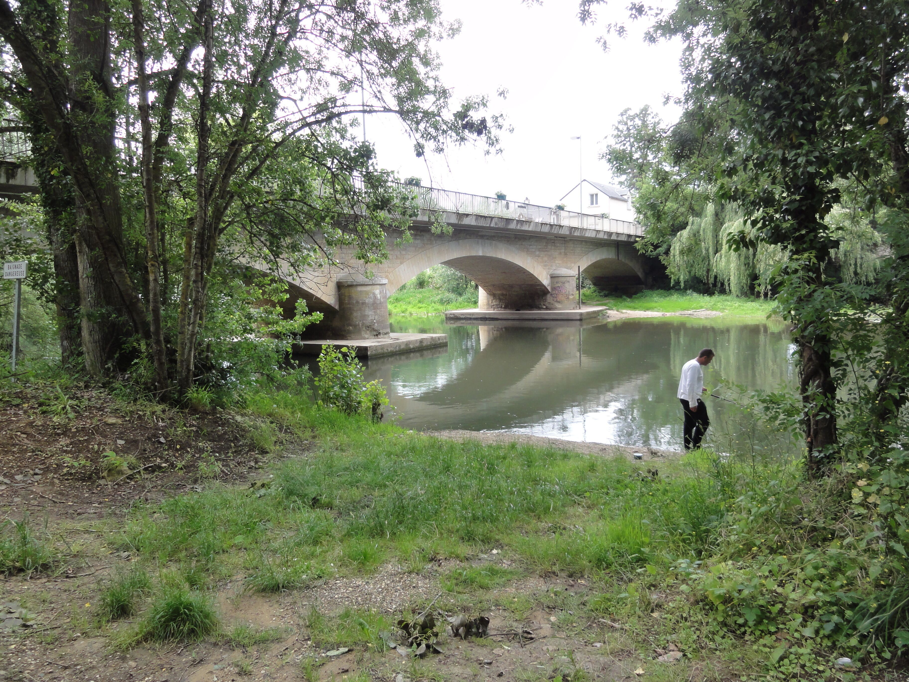 A bridge over a calm river, surrounded by lush greenery and trees.
