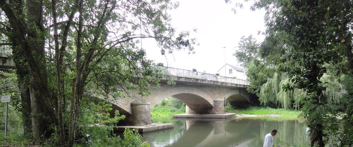 A bridge over a calm river, surrounded by lush greenery and trees.