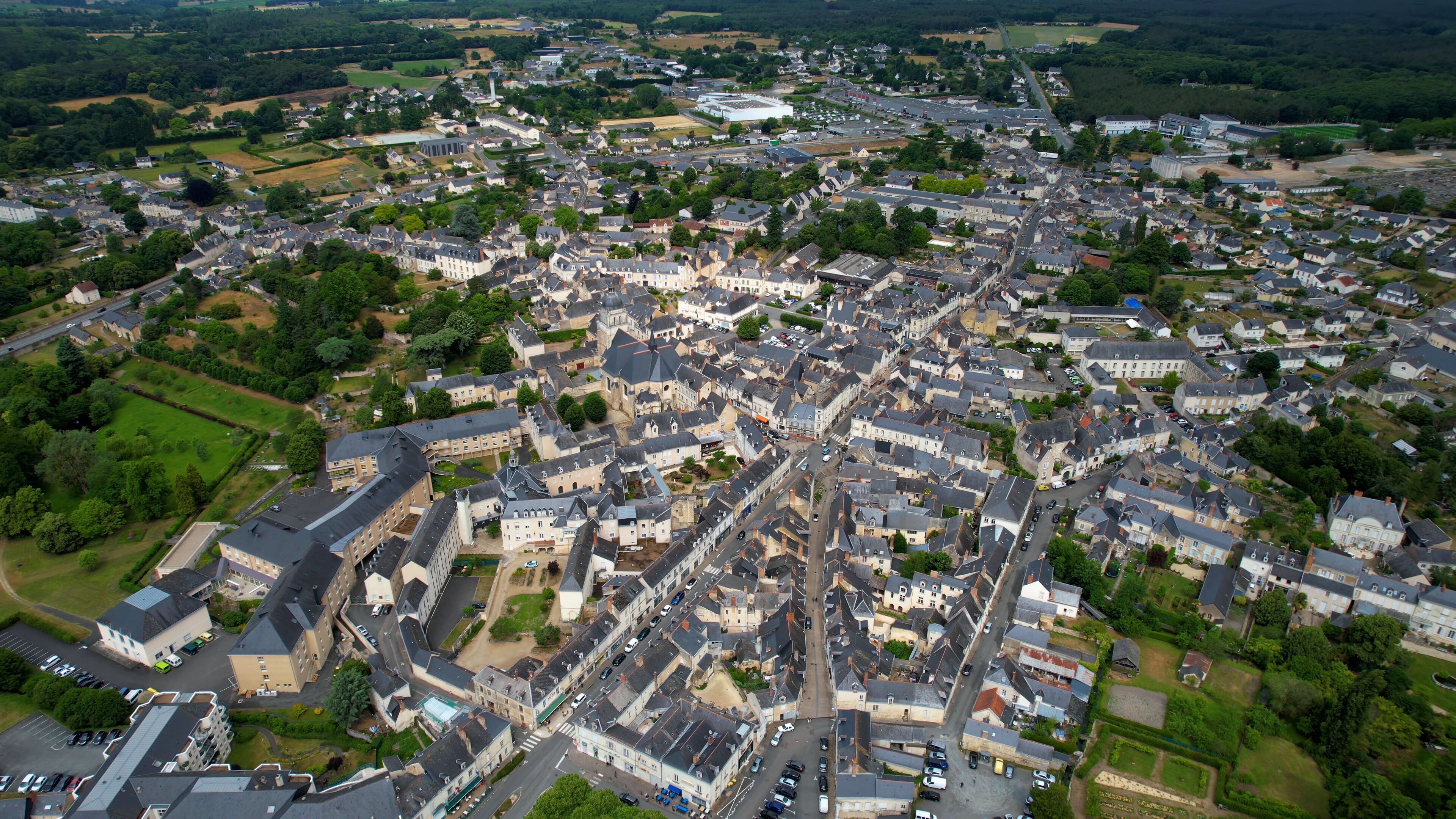 An aerial view of a densely built town with historic architecture, surrounded by green fields and a large stadium.
