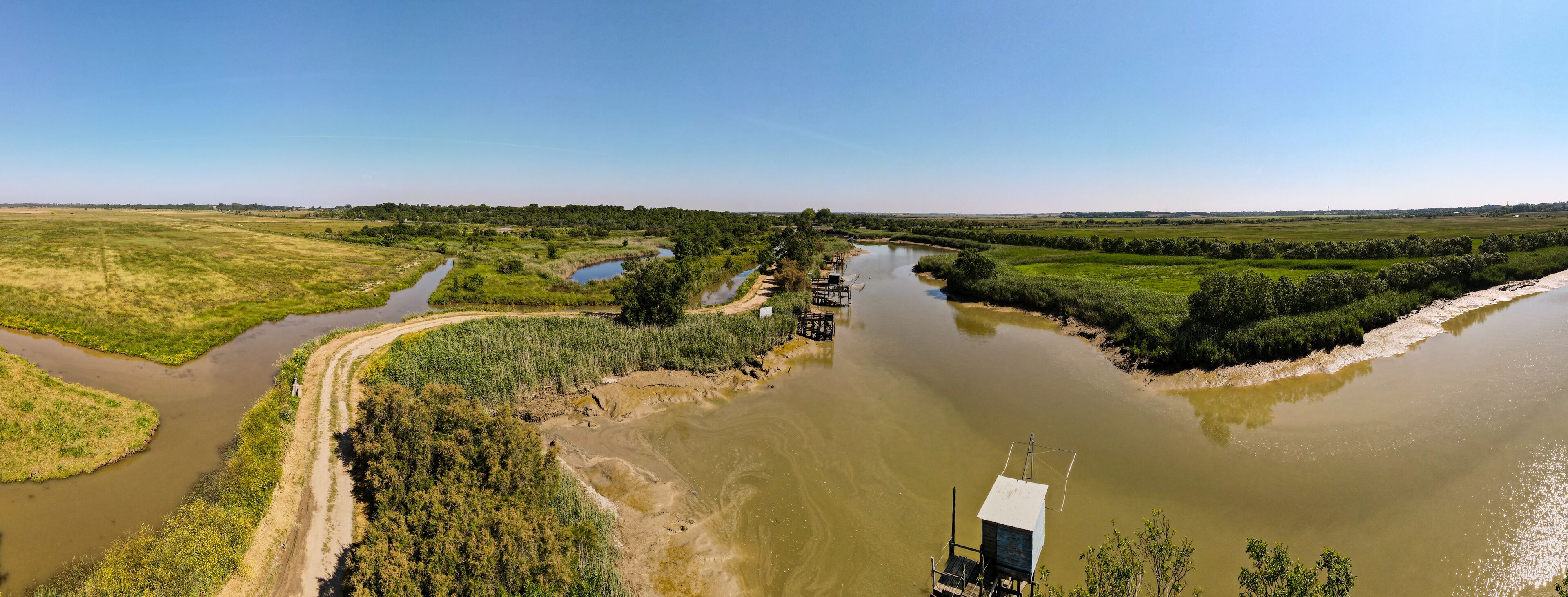 A river meandering through a green landscape with a bridge and a small structure near the water.