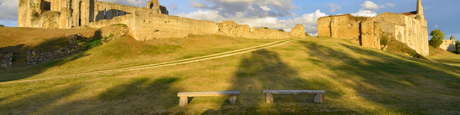 An ancient stone castle with ruins, a grassy hill, and a clear sky.