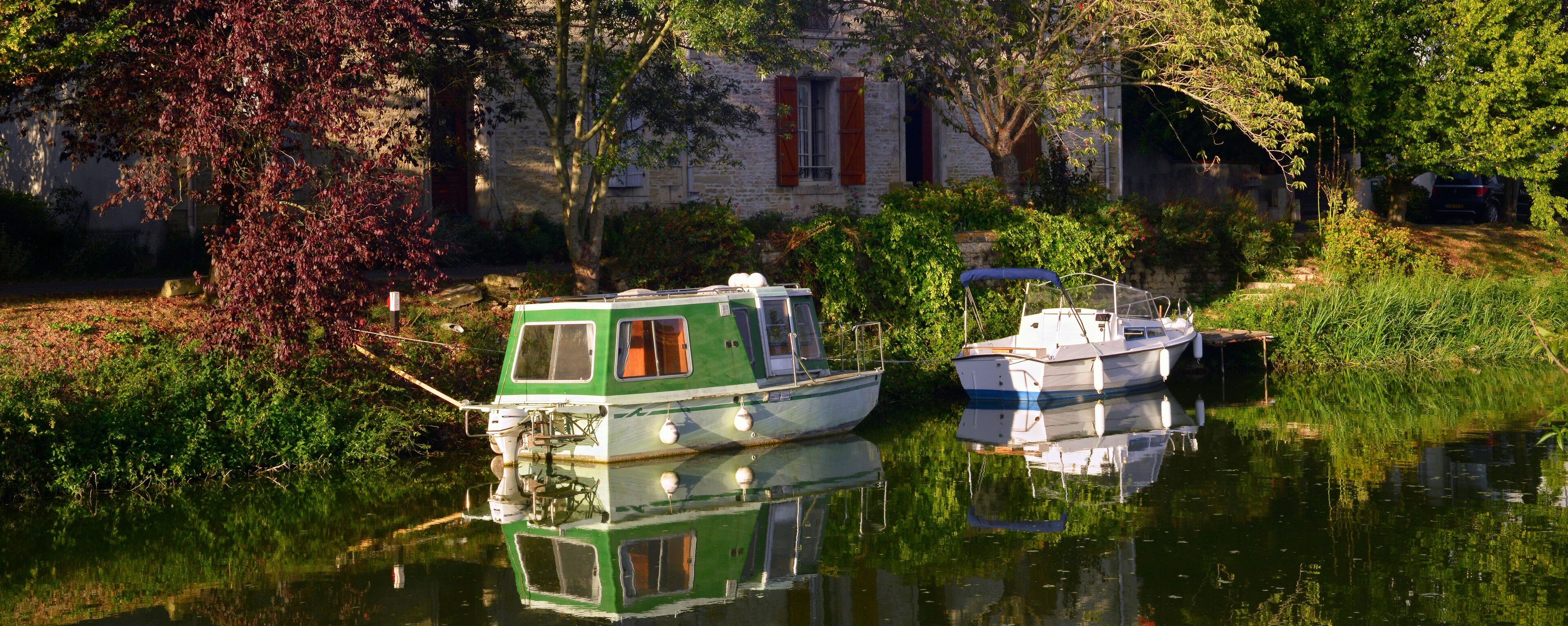 A green and white houseboat docked near a stone building with red shutters.