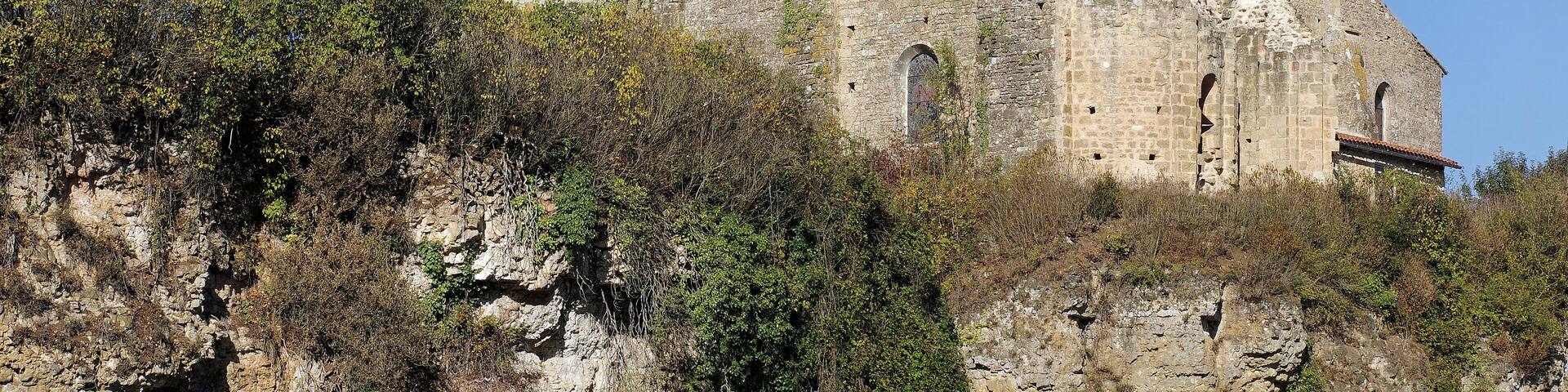 A historic stone castle with a tower, surrounded by greenery and a clear sky.