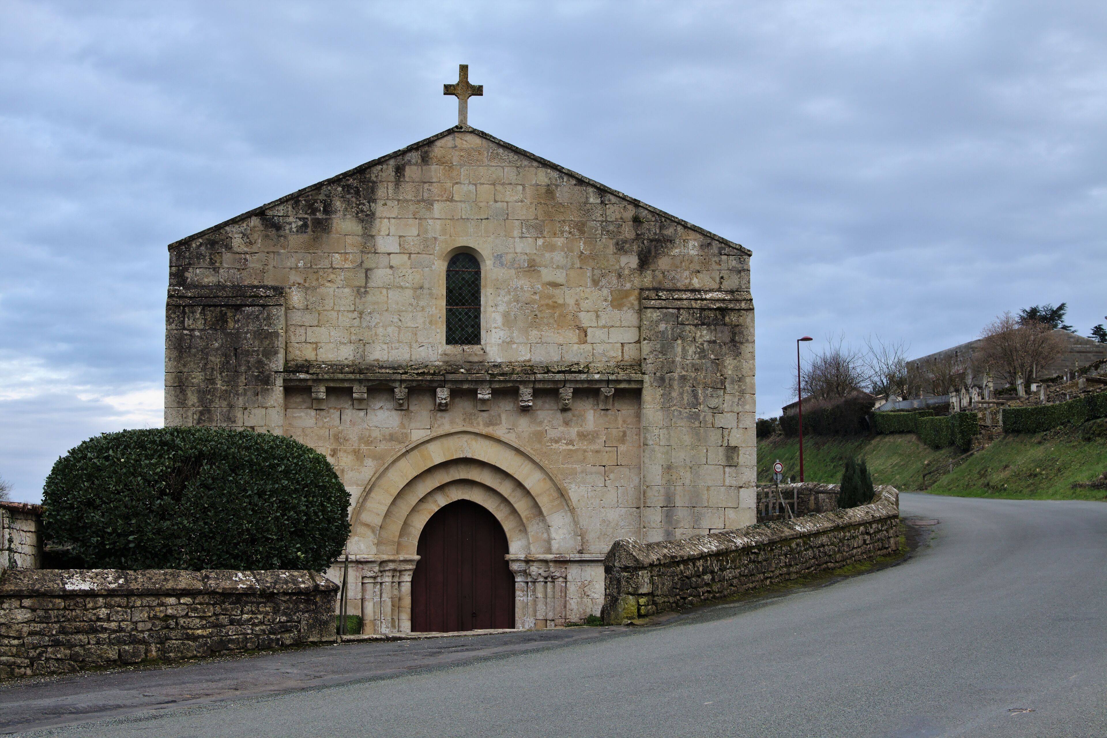A stone church with a cross on top, a large arched entrance, and a small window.