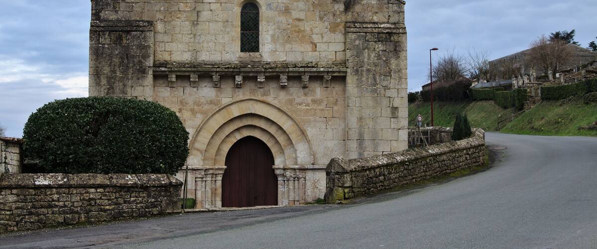 A stone church with a cross on top, a large arched entrance, and a small window.