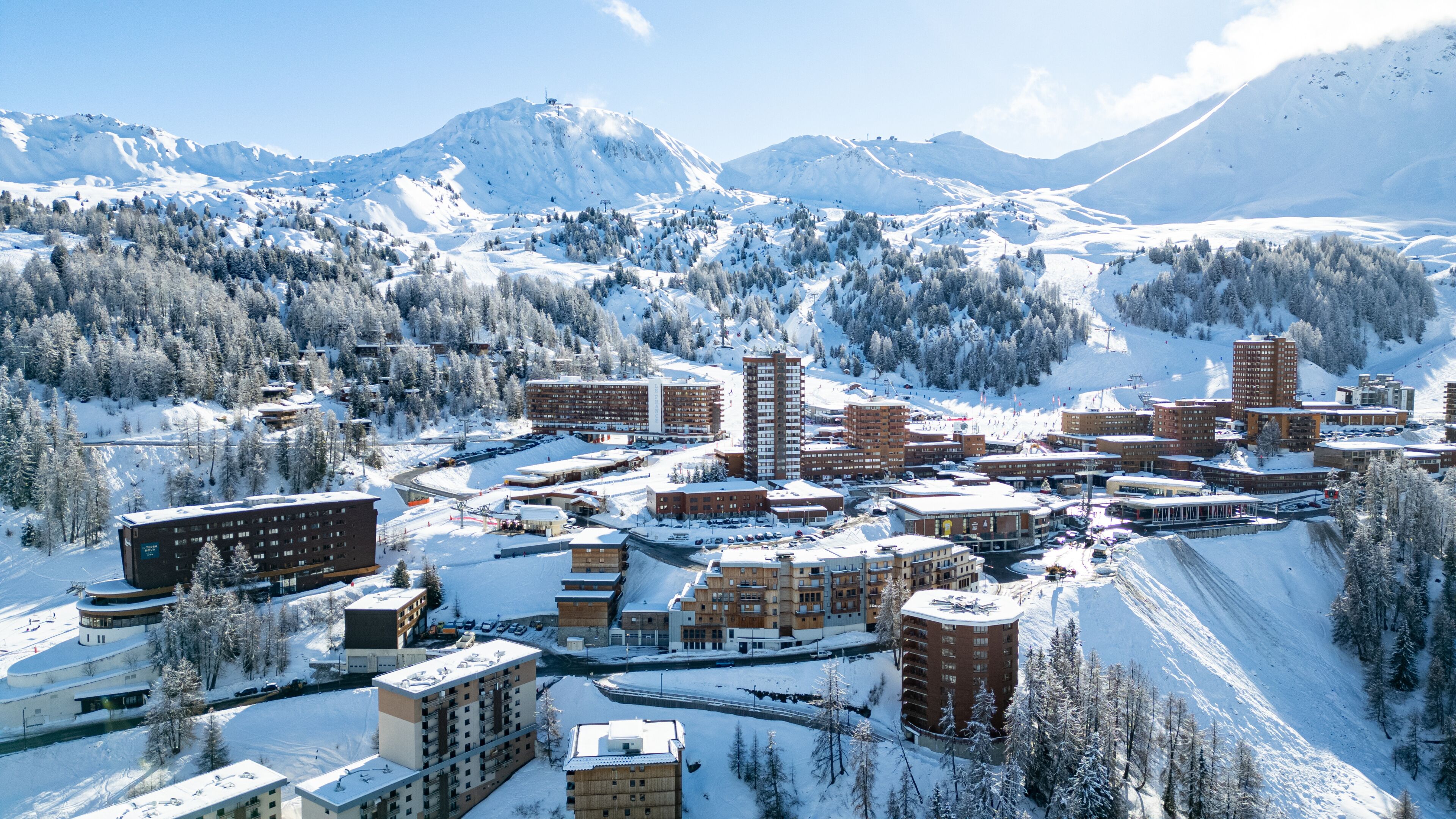 A snow-covered town with buildings, a ski slope, and mountains in the background.