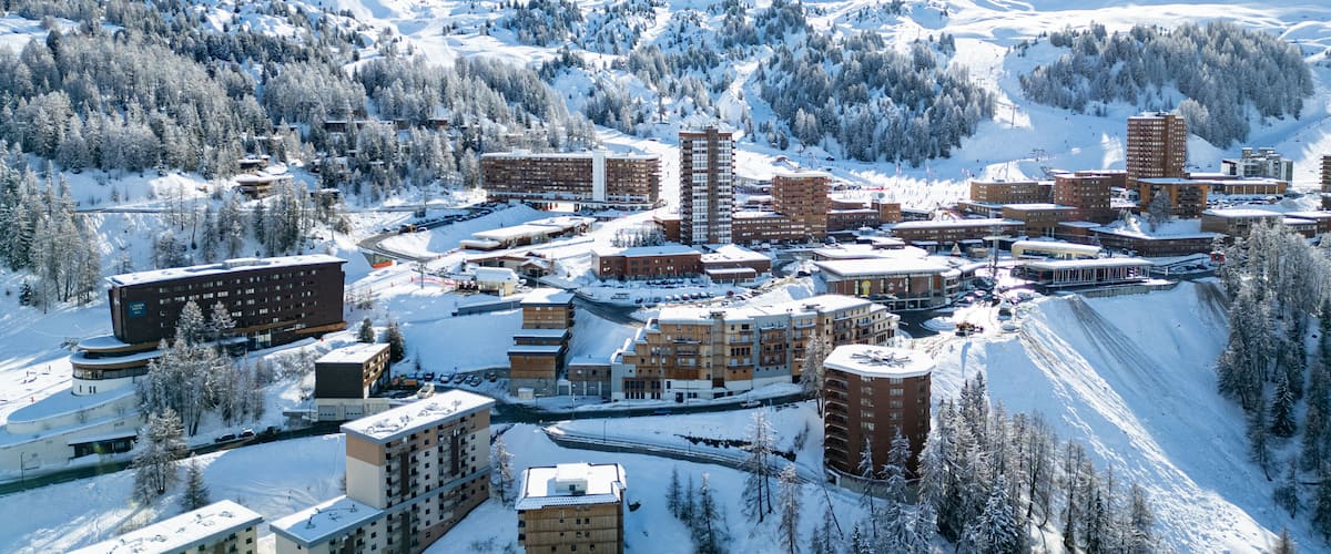 A snow-covered town with buildings, a ski slope, and mountains in the background.