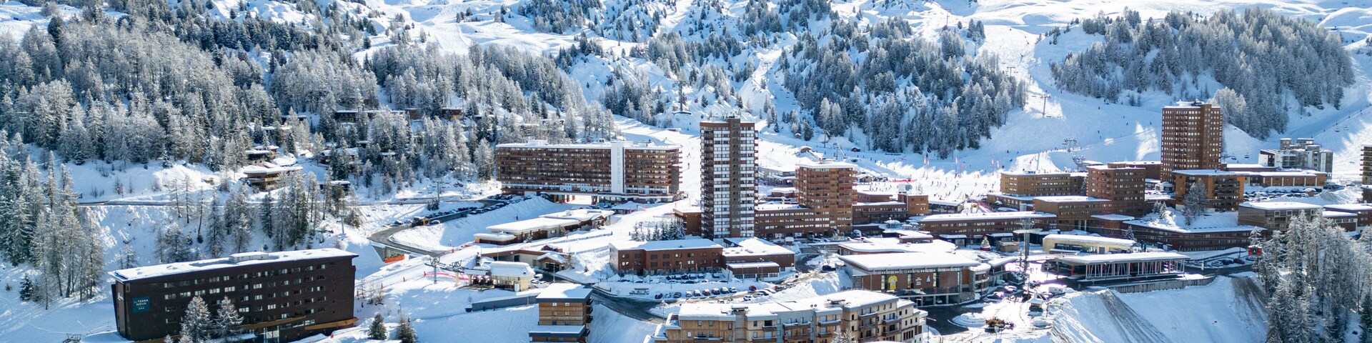 A snow-covered town with buildings, a ski slope, and mountains in the background.