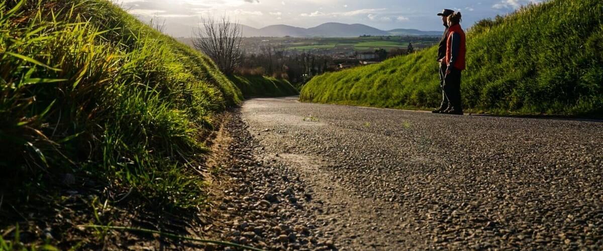 A gravel road flanked by grassy hills under a partly cloudy sky.