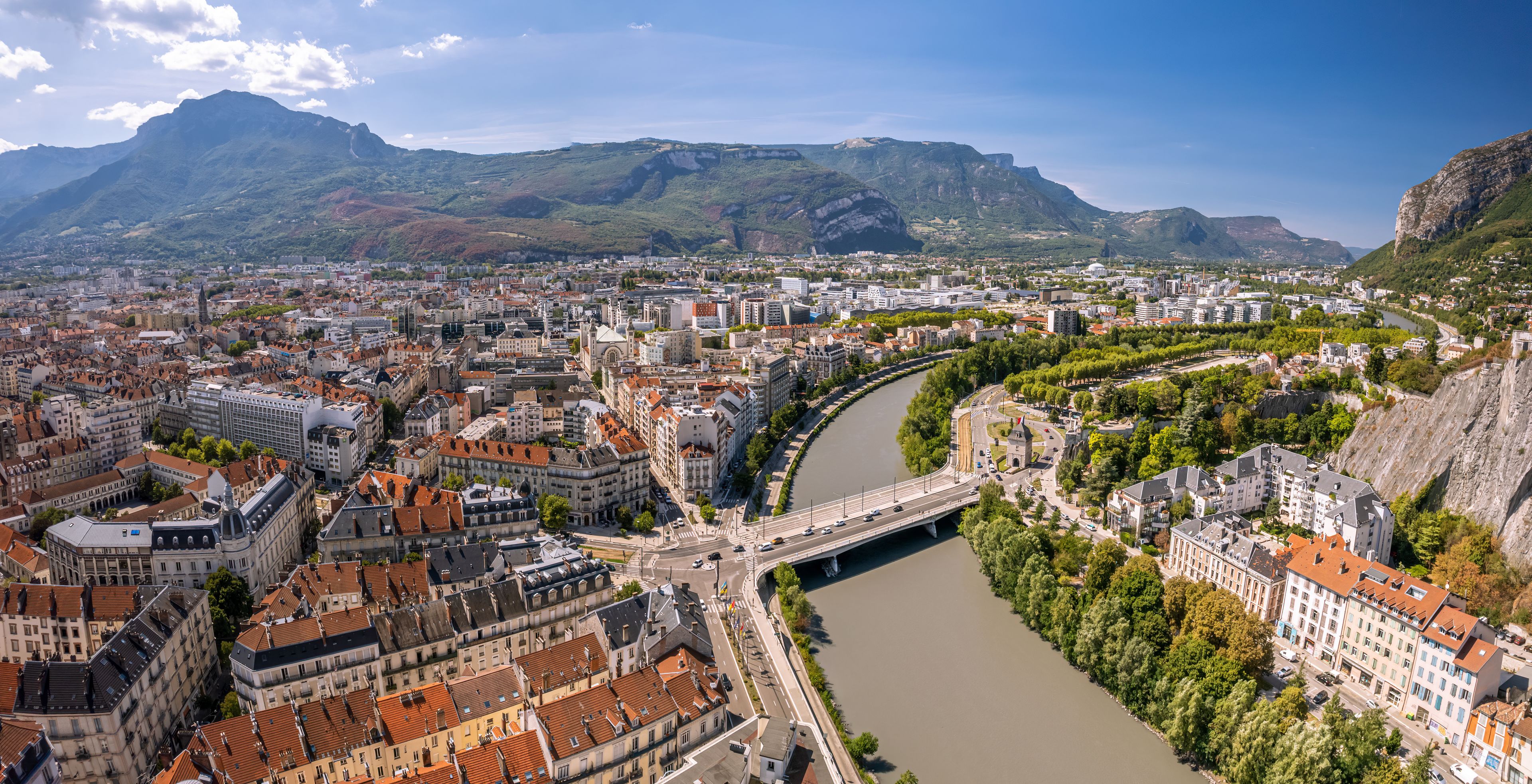 Eine Stadtlandschaft mit einem Fluss, Brücken und Bergen im Hintergrund.