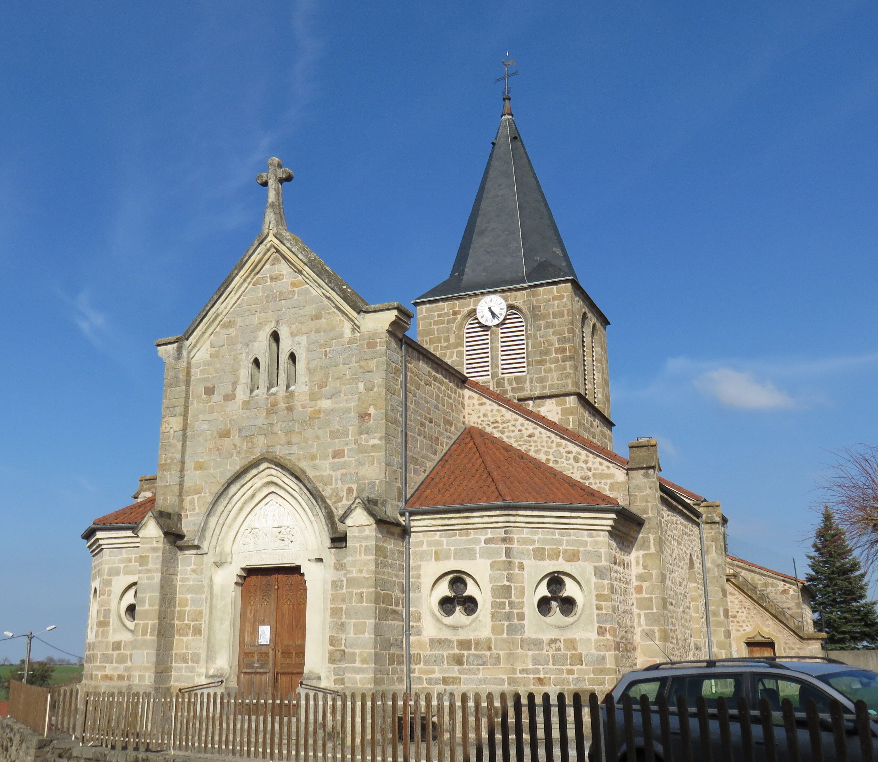A stone church with a clock tower and a wooden fence in front.
