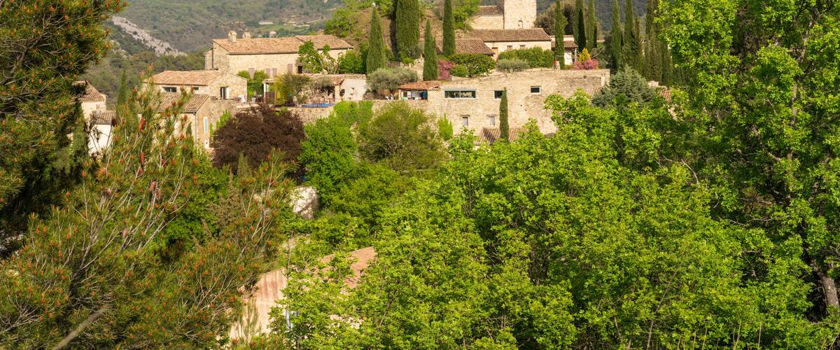 A mountainous village with stone buildings and a tower, surrounded by lush greenery and hills.