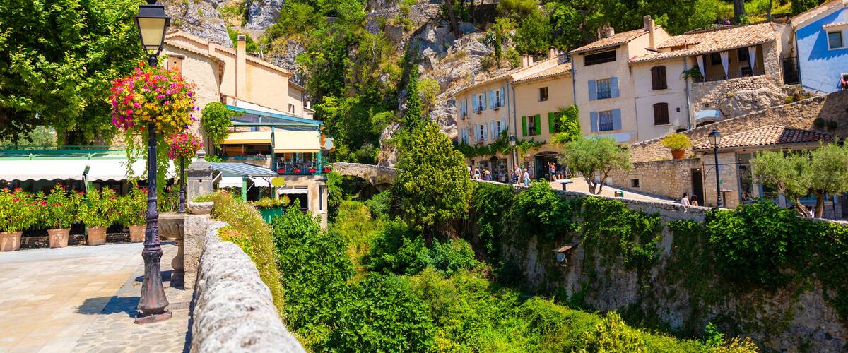 A scenic village with stone buildings, lush greenery, and a rocky mountain backdrop.