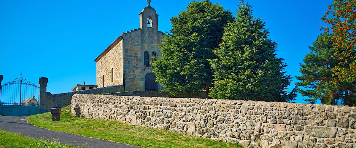 A stone church with a bell tower, surrounded by trees and a stone wall.
