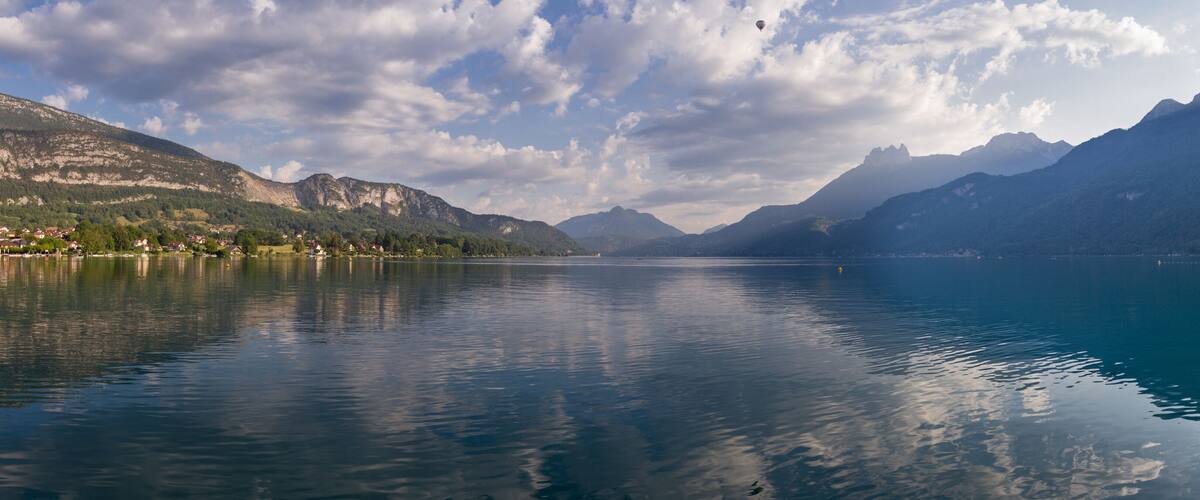 A calm lake with mountains in the background and a partly cloudy sky.
