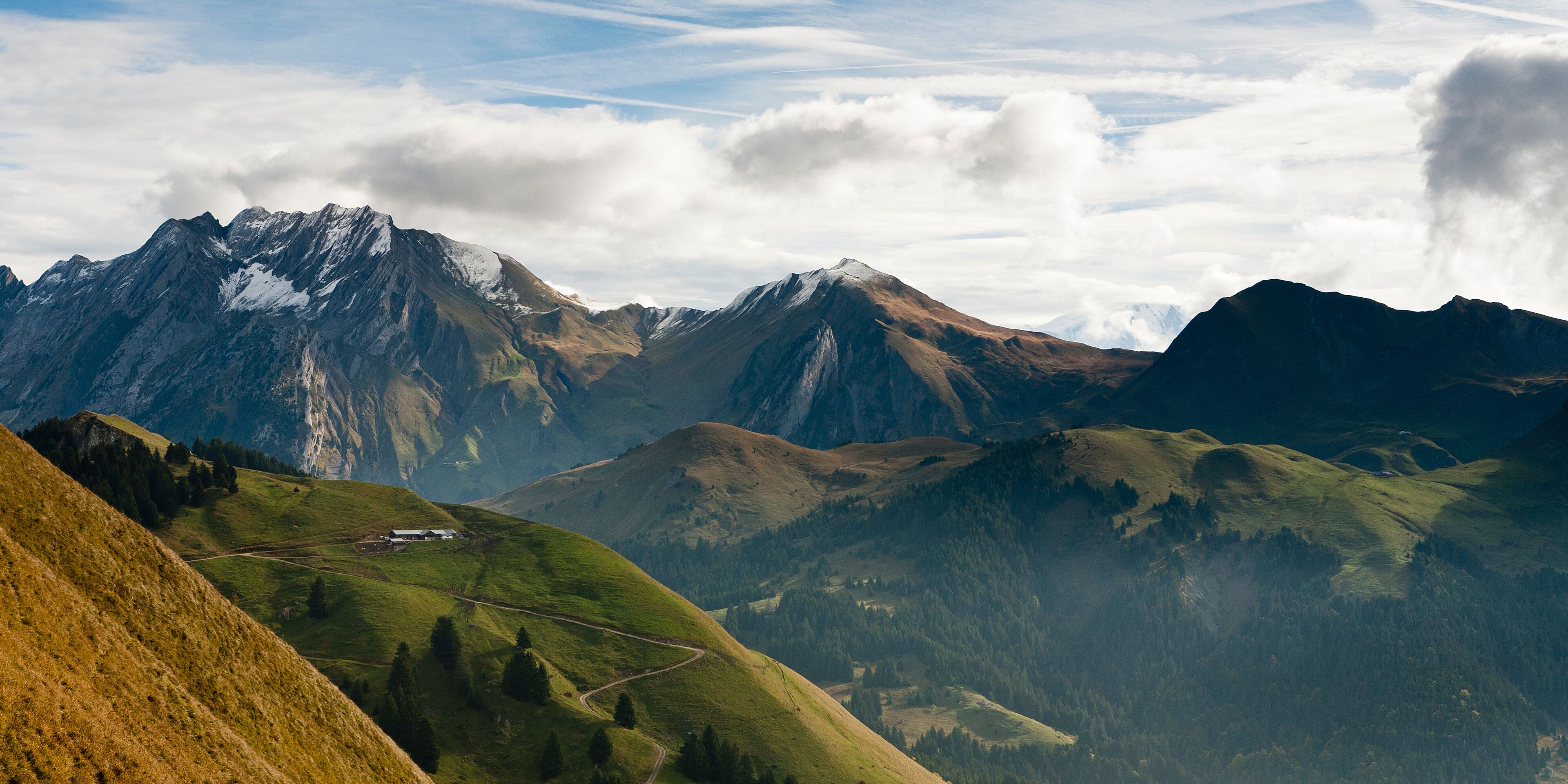 A mountain landscape with a winding road, snow-capped peaks, and a valley.