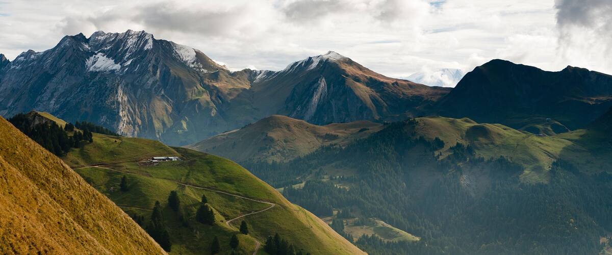 A mountain landscape with a winding road, snow-capped peaks, and a valley.