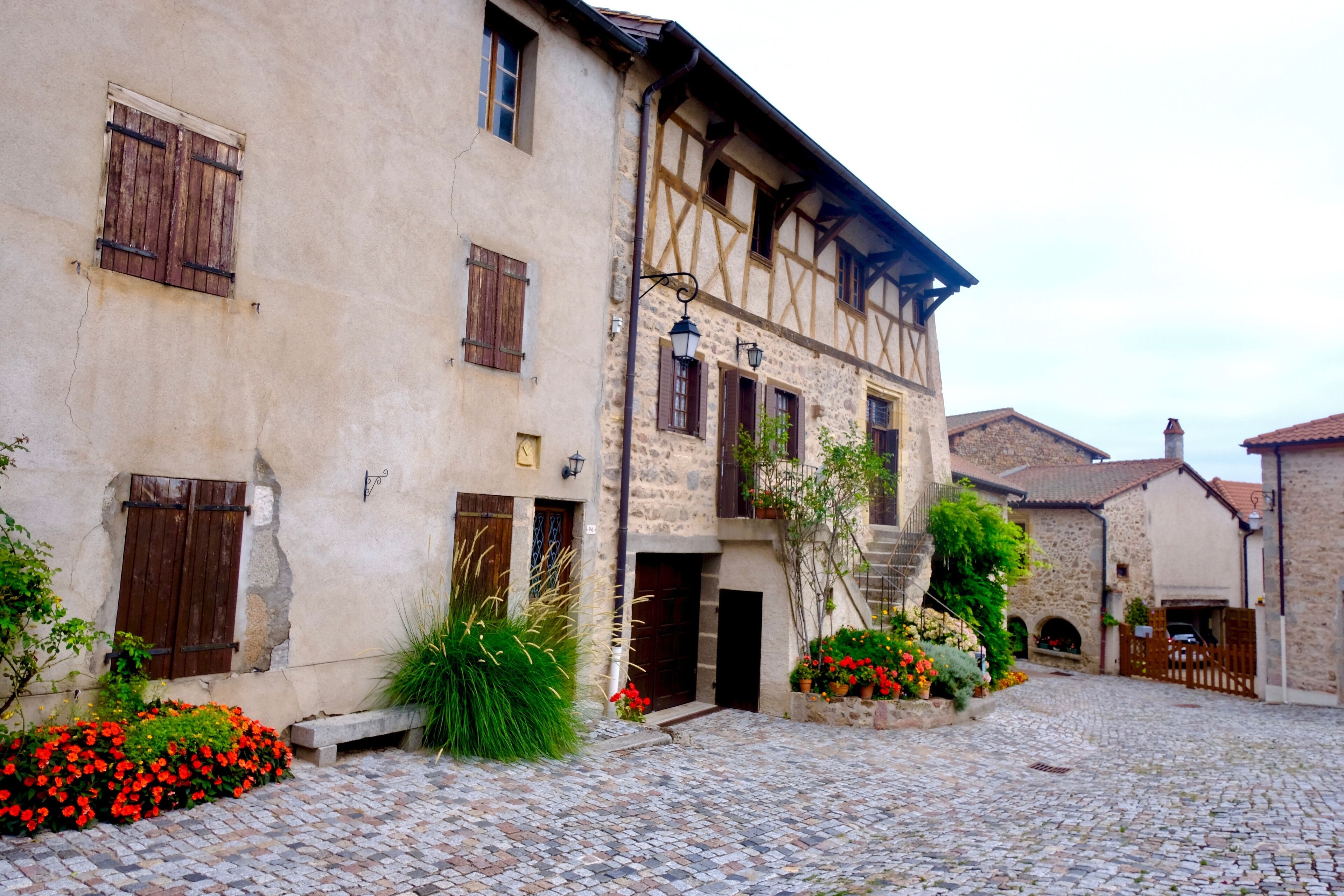 A cobblestone courtyard with a half-timbered building, wooden shutters, and flowering plants.