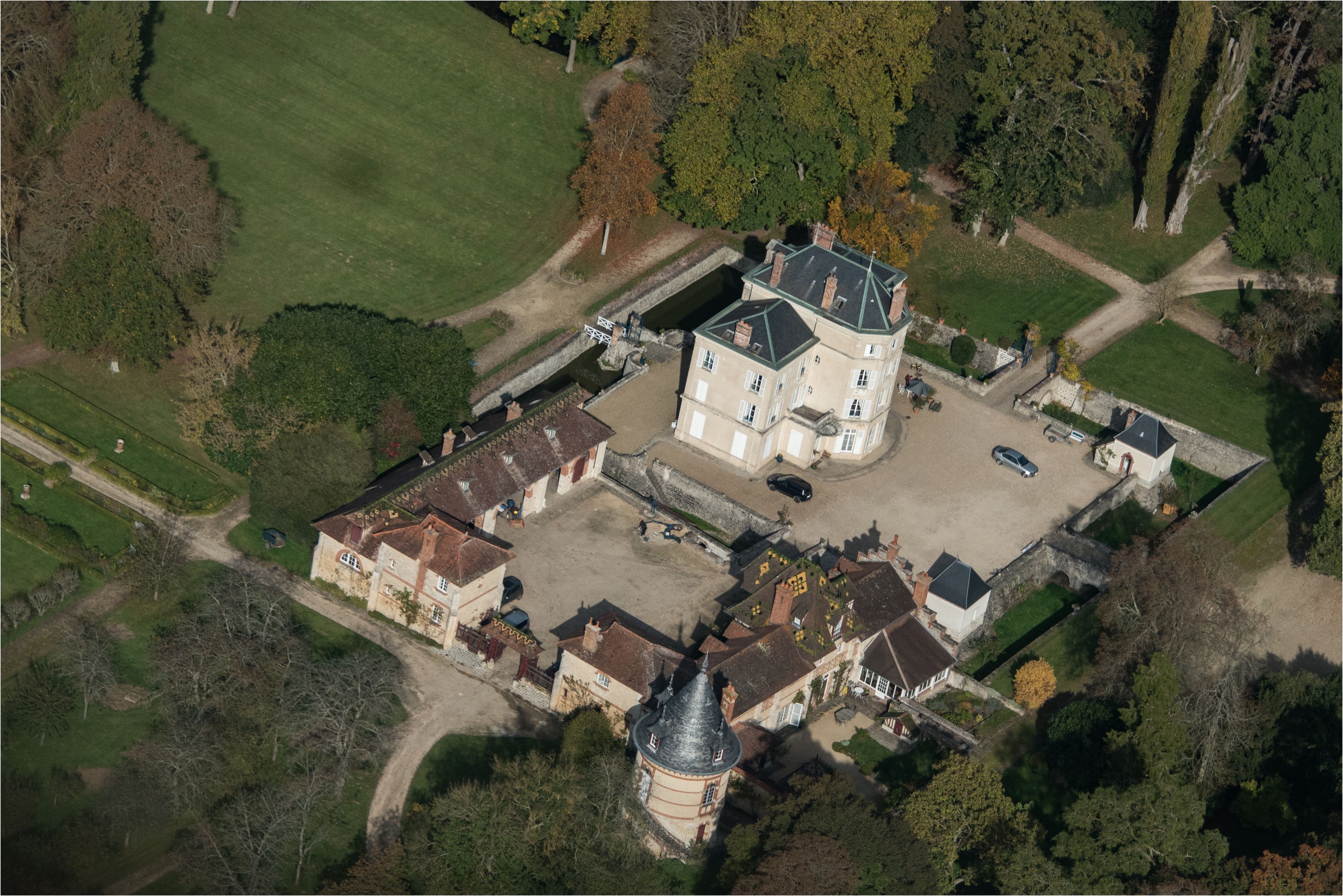 Luchtbeeld van een groot landgoed met een centraal gebouw, een toren en omliggende tuinen.