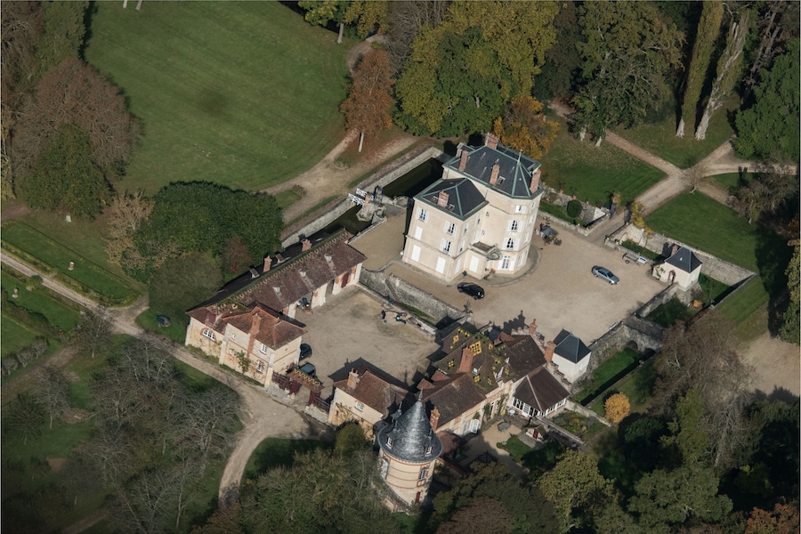 Luchtbeeld van een groot landgoed met een centraal gebouw, een toren en omliggende tuinen.