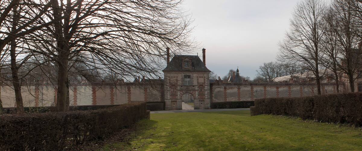 A historic building with a tower, surrounded by hedges and leafless trees.