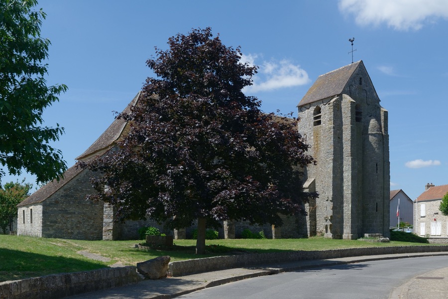 A stone church with a bell tower, surrounded by a grassy area and trees.