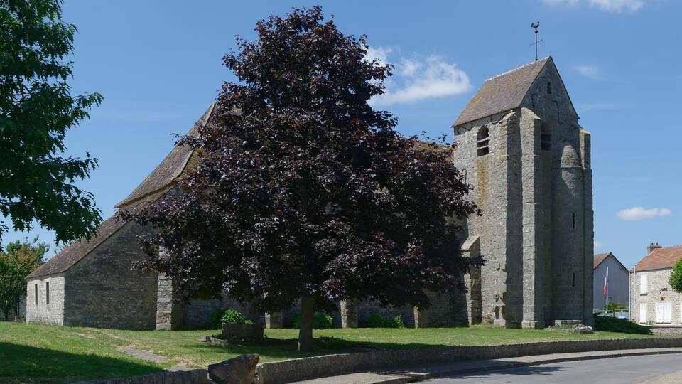 A stone church with a bell tower, surrounded by a grassy area and trees.