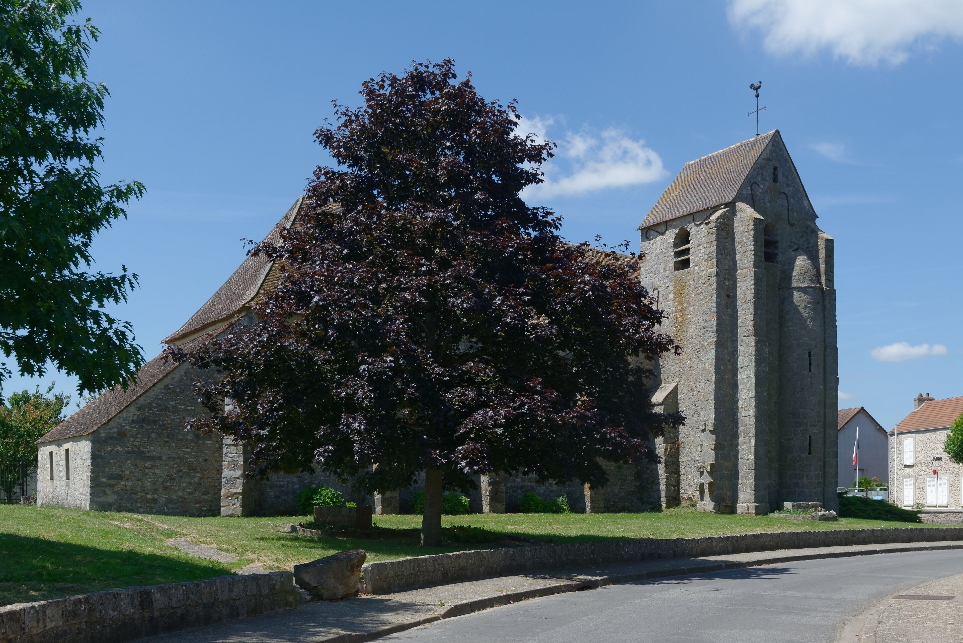 A stone church with a bell tower, surrounded by a grassy area and trees.