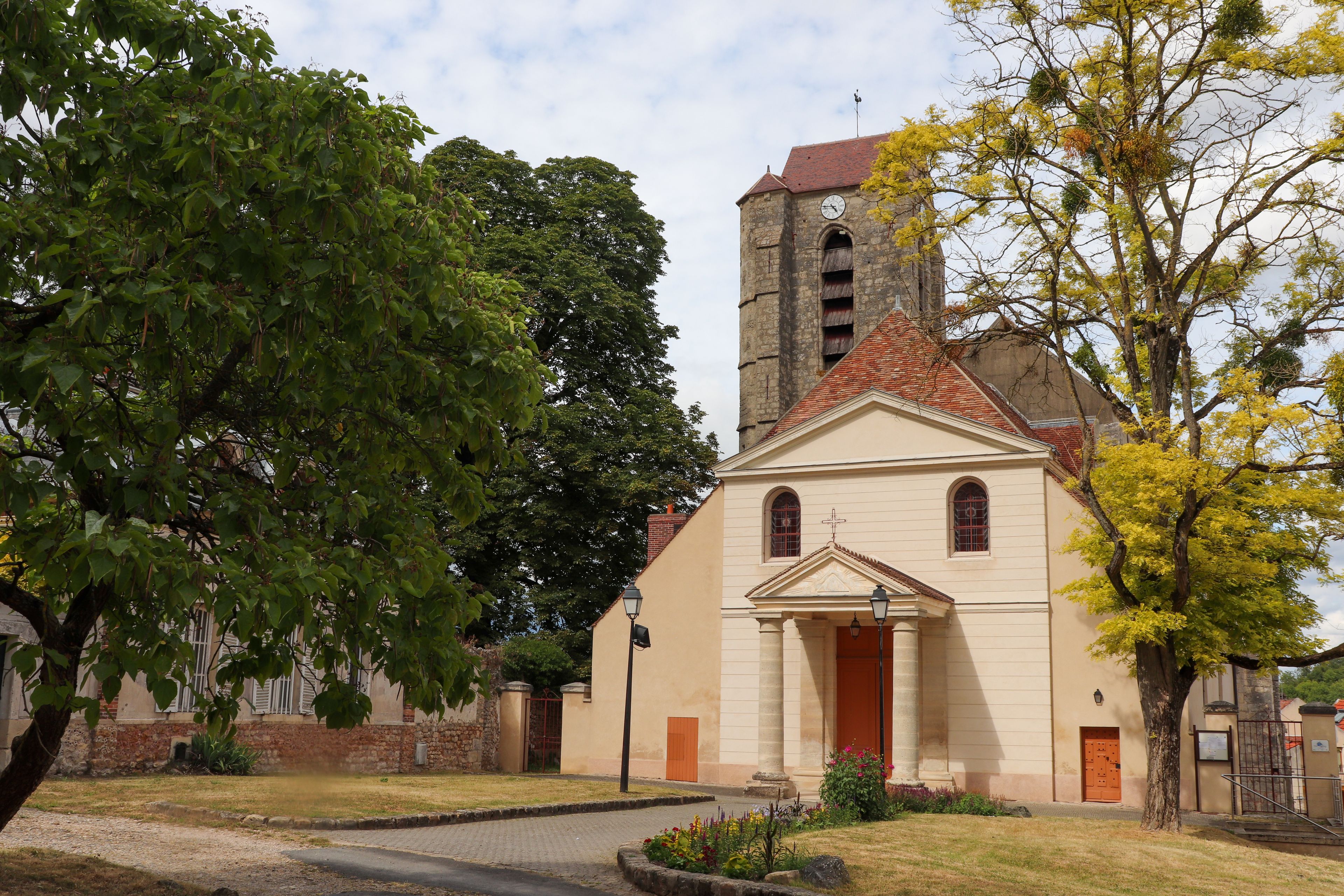 Una iglesia con un campanario, rodeada de árboles y un patio empedrado.