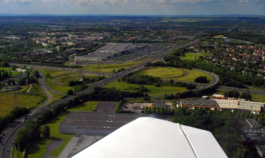An aerial view of a city with a large industrial area, multiple highways, and surrounding green spaces.