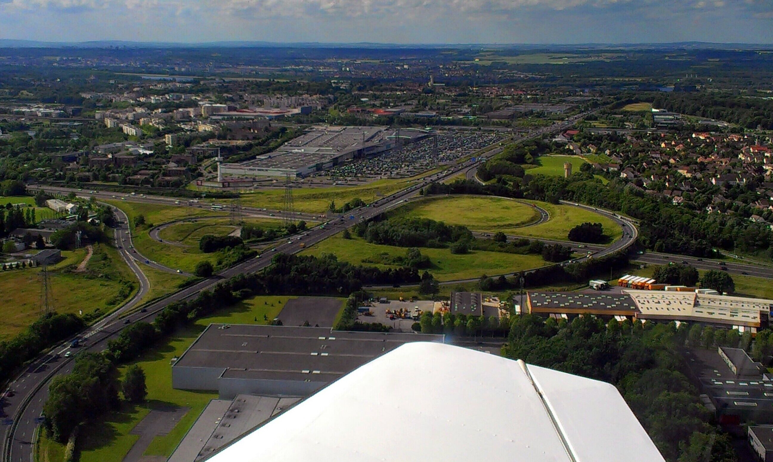 An aerial view of a city with a large industrial area, multiple highways, and surrounding green spaces.