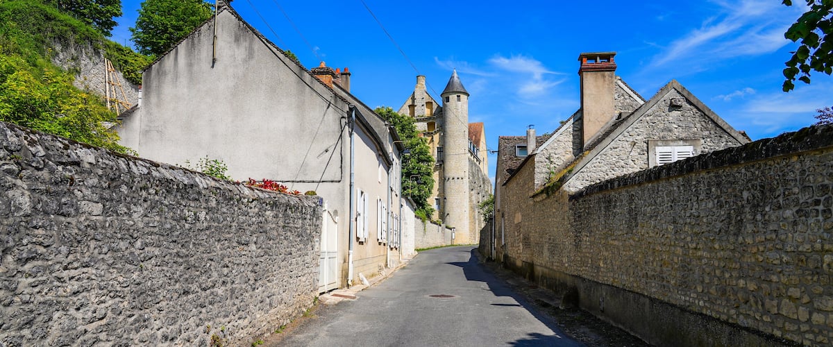 A narrow stone street flanked by historic buildings with a prominent tower.