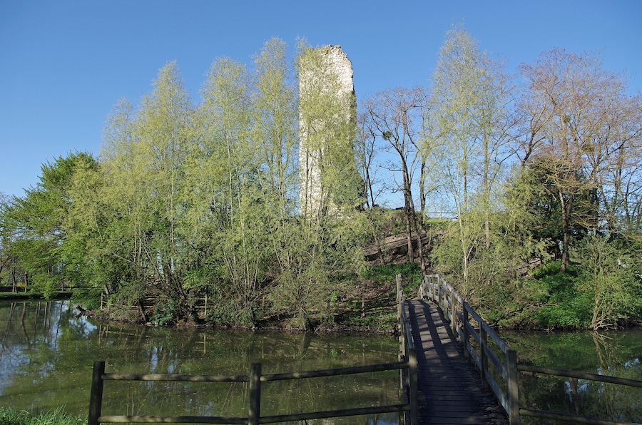 A wooden bridge over a calm river, surrounded by lush greenery and a tall, ancient stone structure.