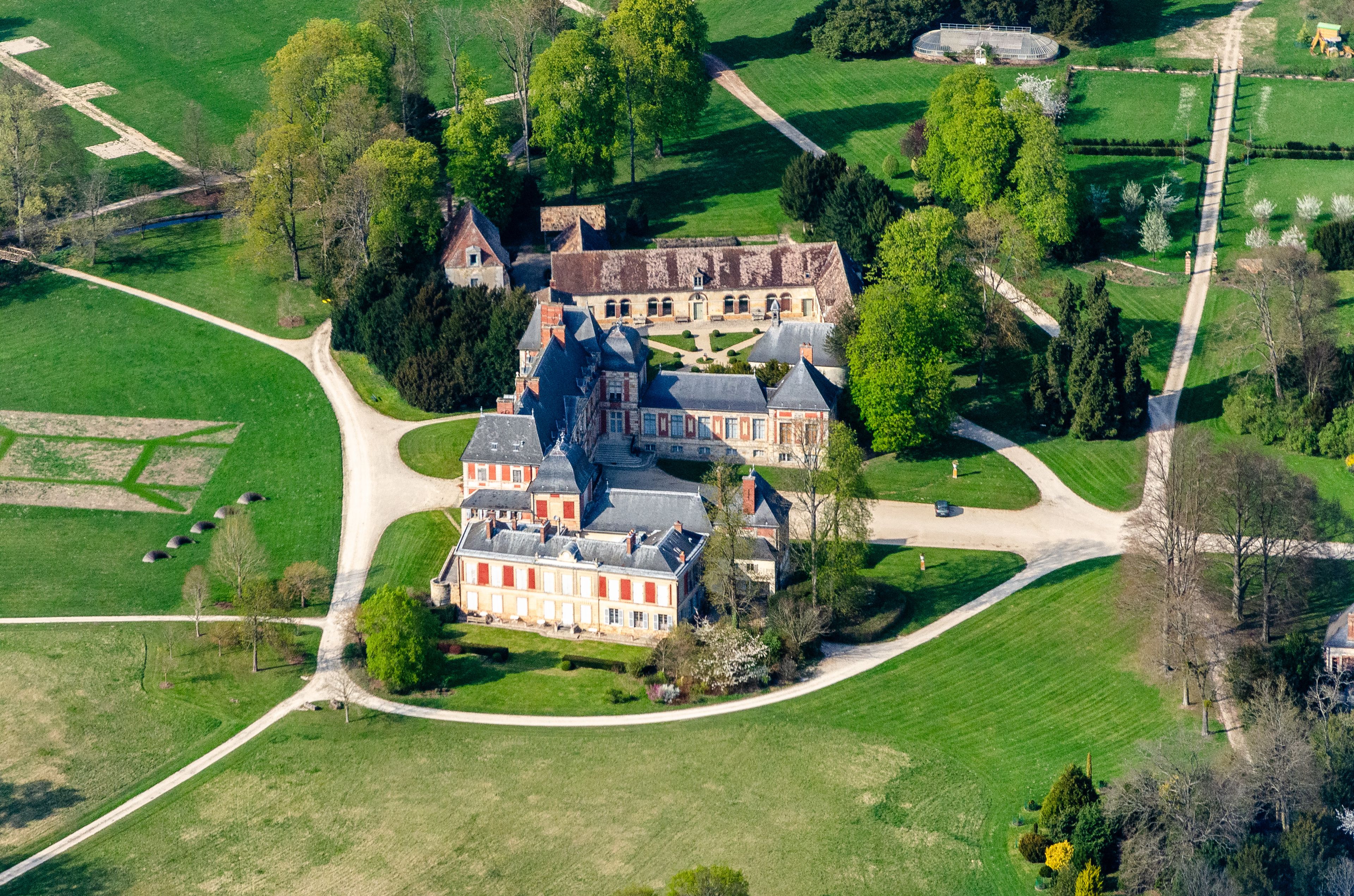 An aerial view of a large estate with a prominent building, surrounded by well-maintained gardens and open fields.
