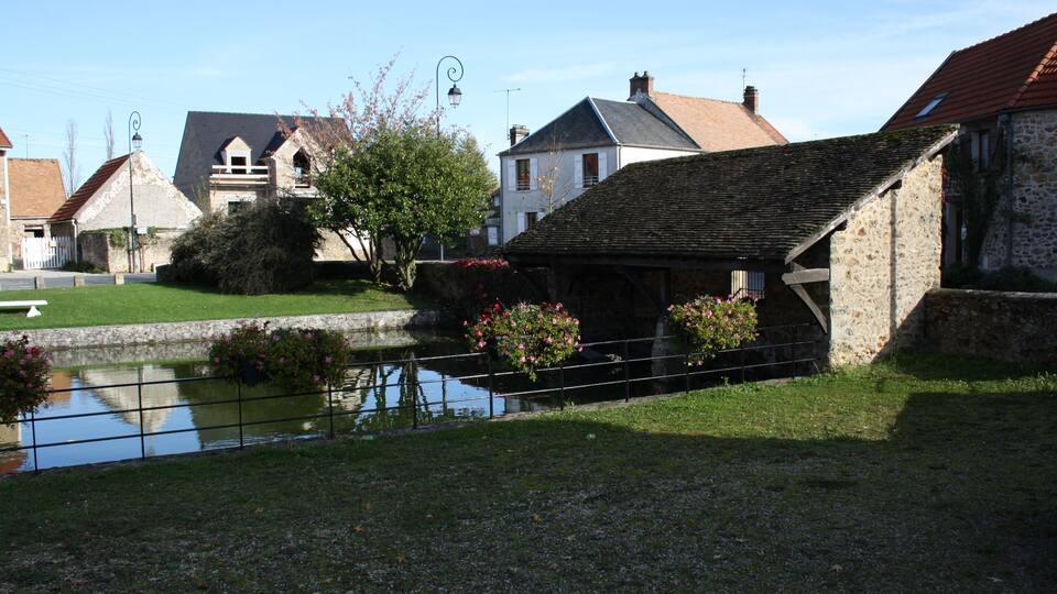 A serene village scene with stone buildings, a small pond, and blooming flowers.