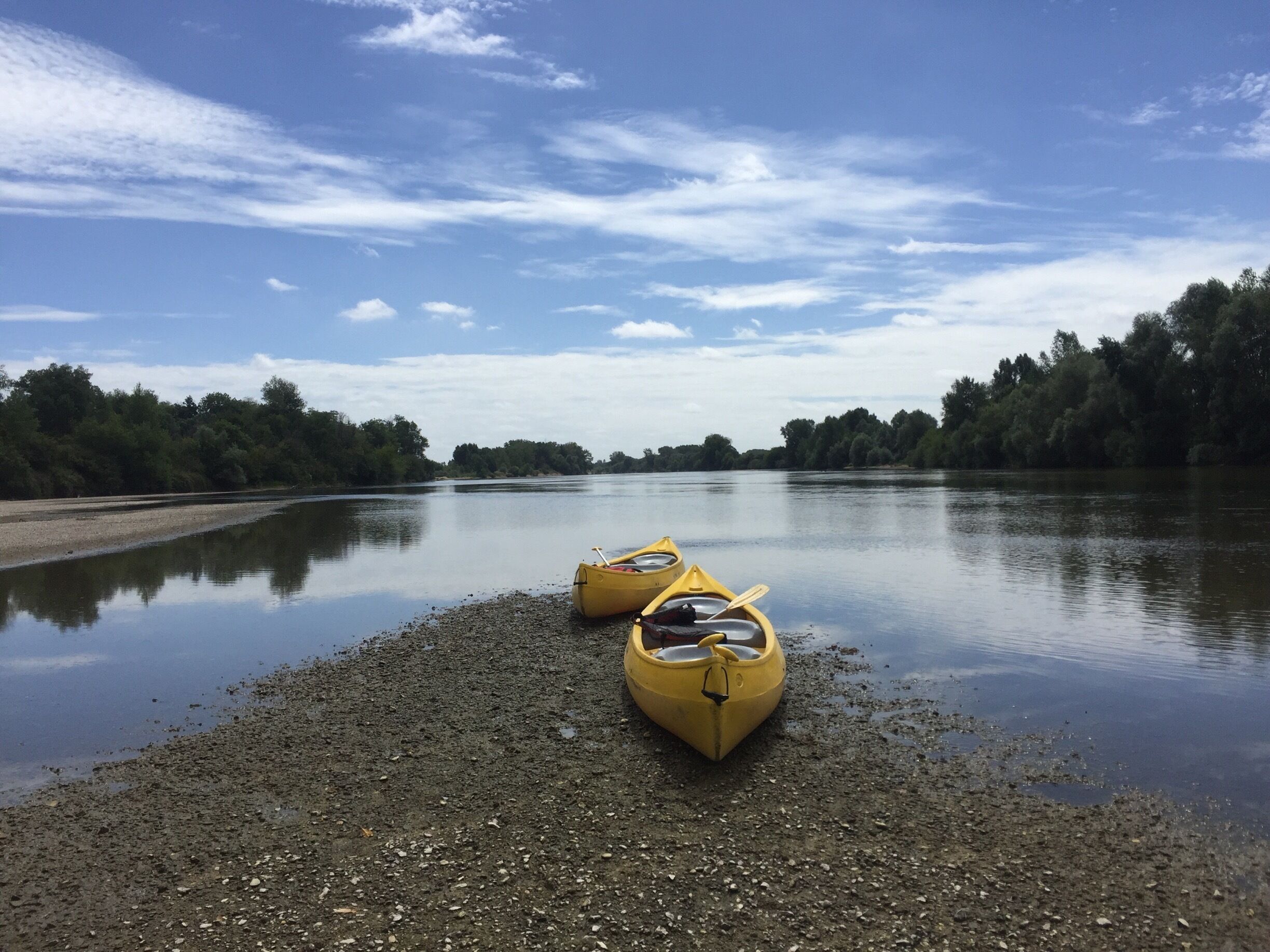 A calm river with two yellow kayaks on a pebbly shore.