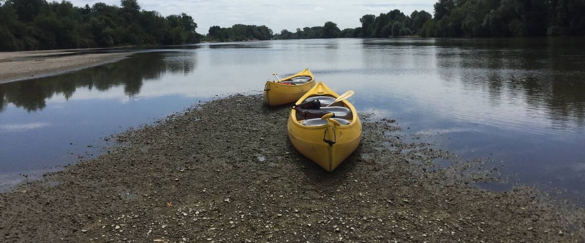 A calm river with two yellow kayaks on a pebbly shore.