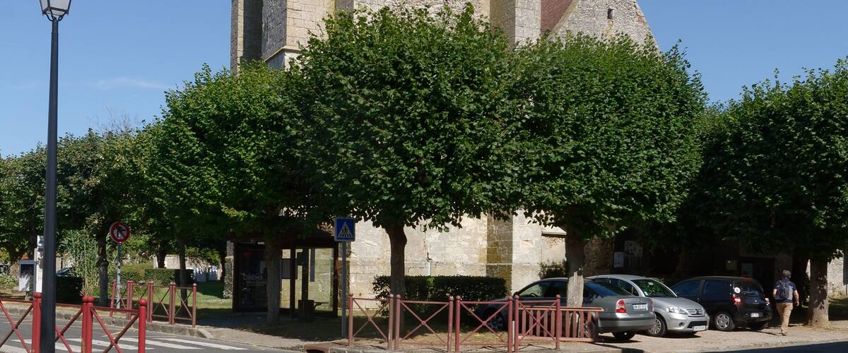 A tall stone church with a clock tower, surrounded by trees and parked cars.