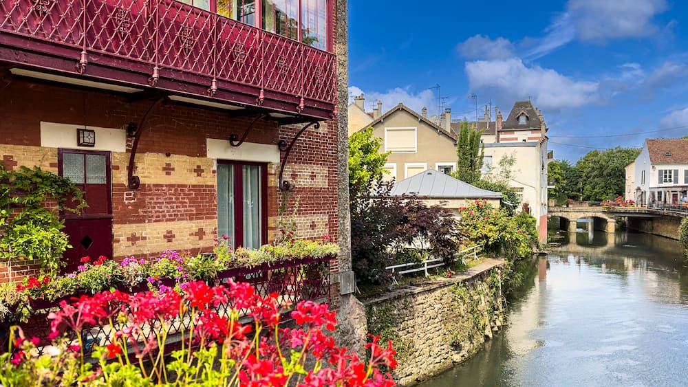 Un canal surmonté d’un pont, un balcon rouge et des fleurs en pleine floraison le long des berges.