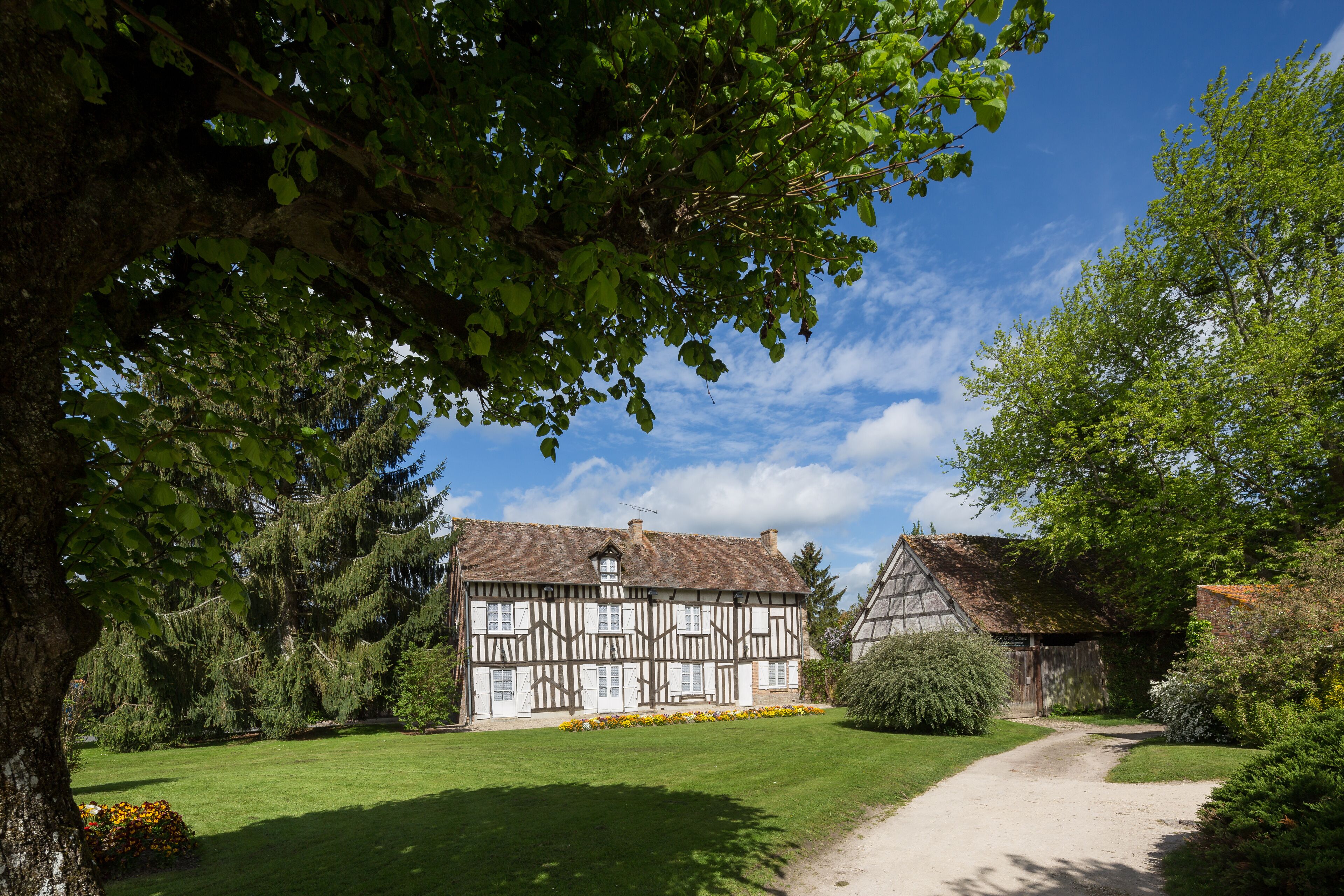 A traditional half-timbered house with a well-maintained lawn and a gravel path leading to it.
