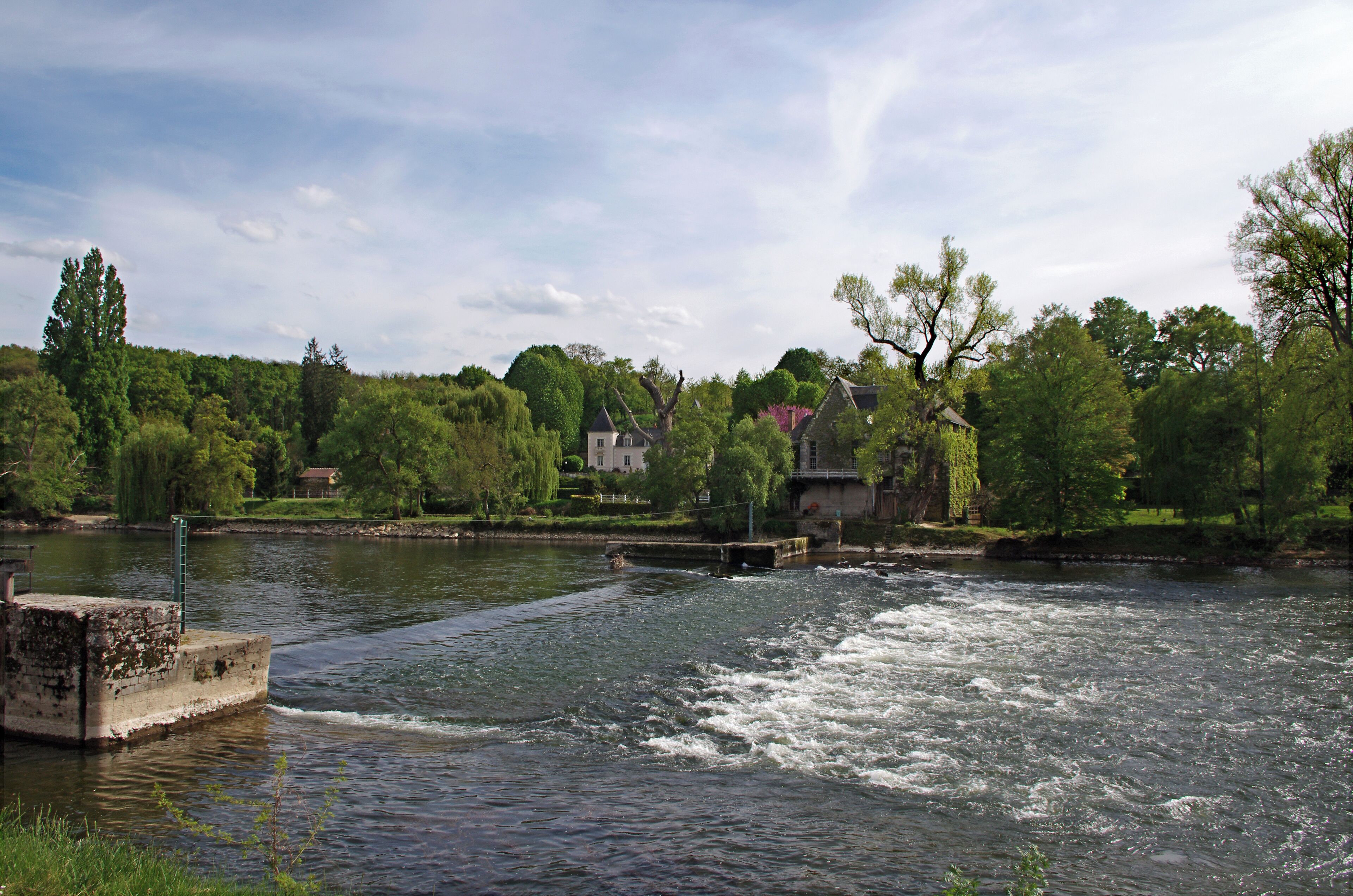 A river with a bridge, surrounded by lush greenery and houses.