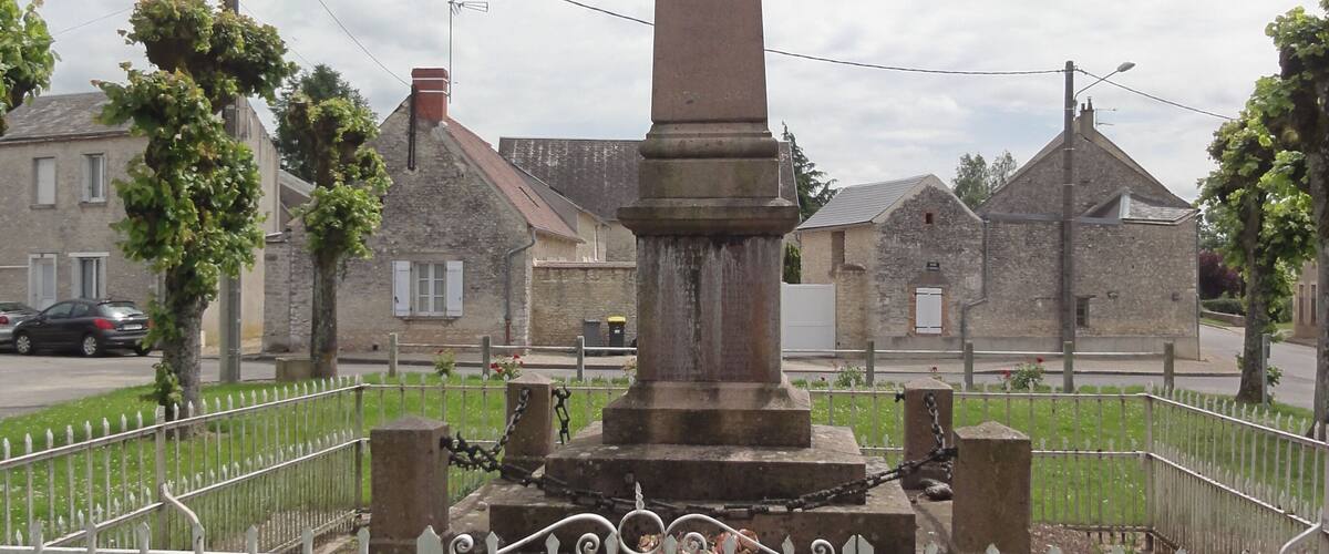 A tall stone monument with a cross on top, surrounded by a white fence and a grassy area.