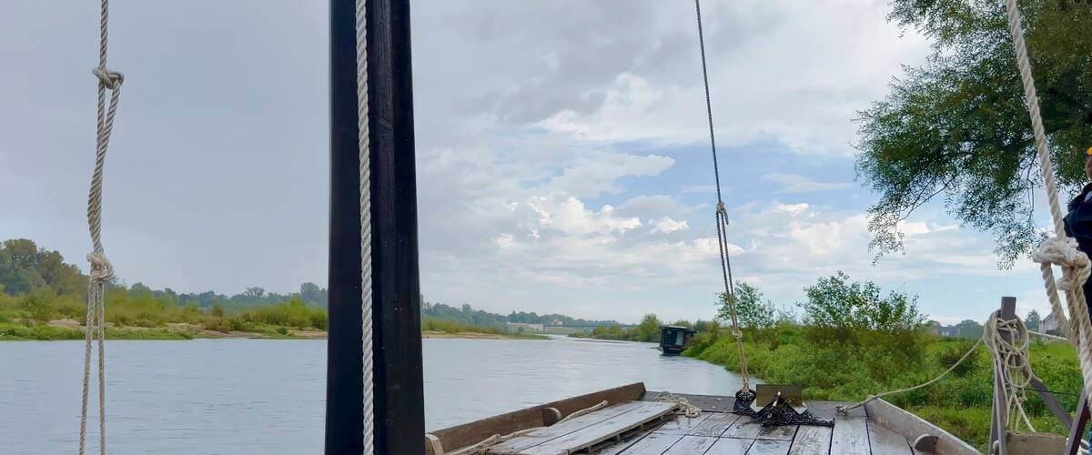 A wooden boat with ropes tied to a pole, a river, and greenery in the background.