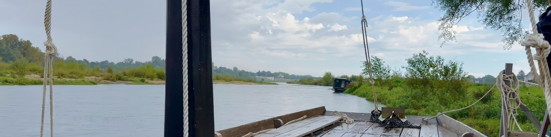 A wooden boat with ropes tied to a pole, a river, and greenery in the background.