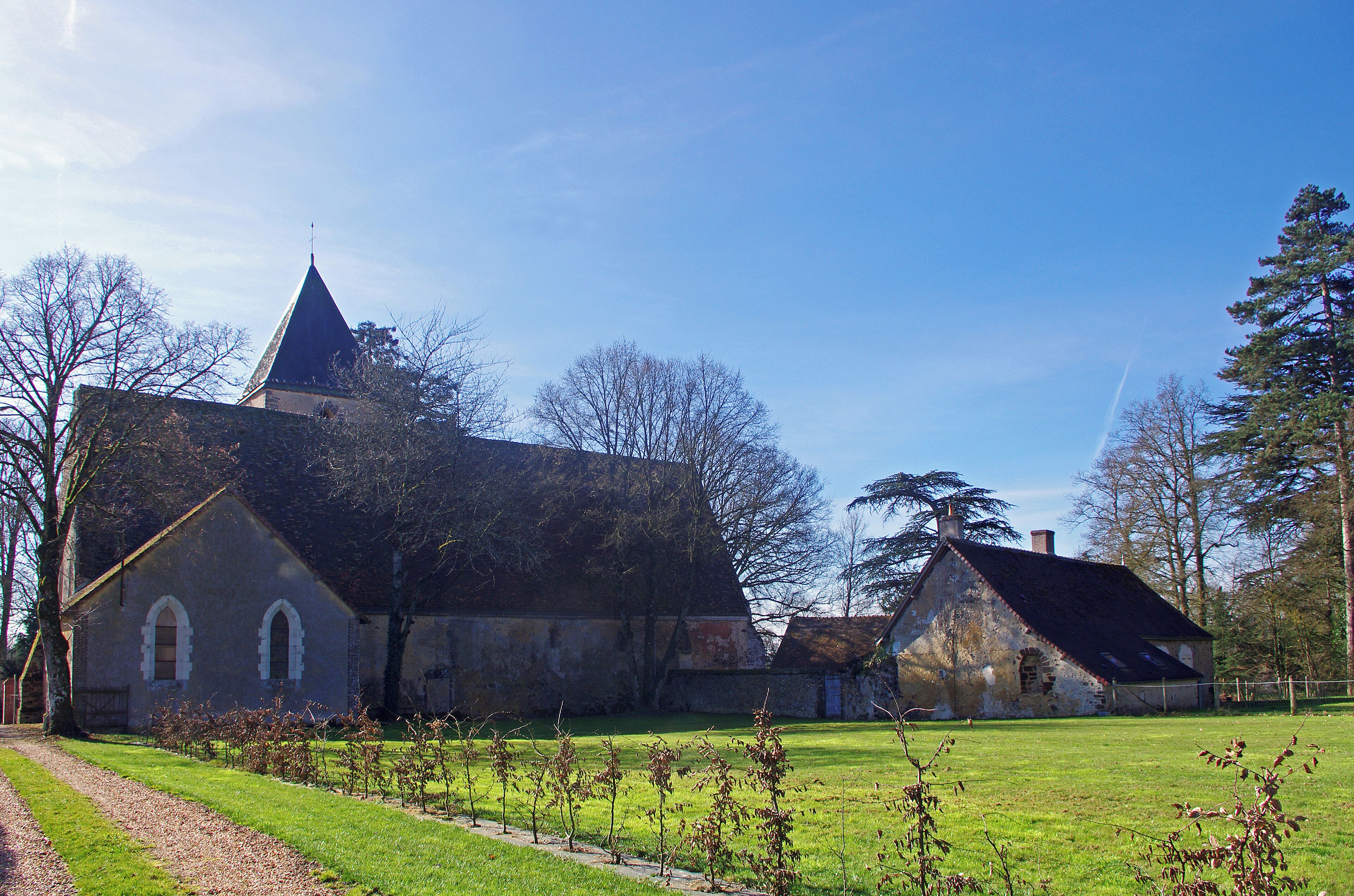 A historic church with a pointed steeple, surrounded by a grassy field and trees.