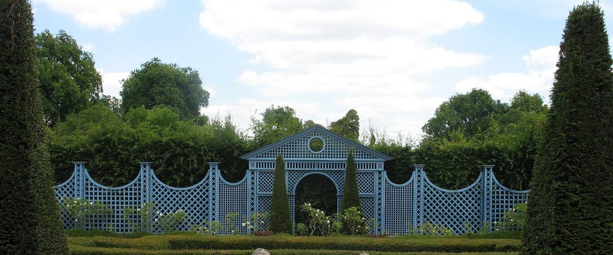 A garden with a blue lattice fence, two stone statues, and a building in the background.