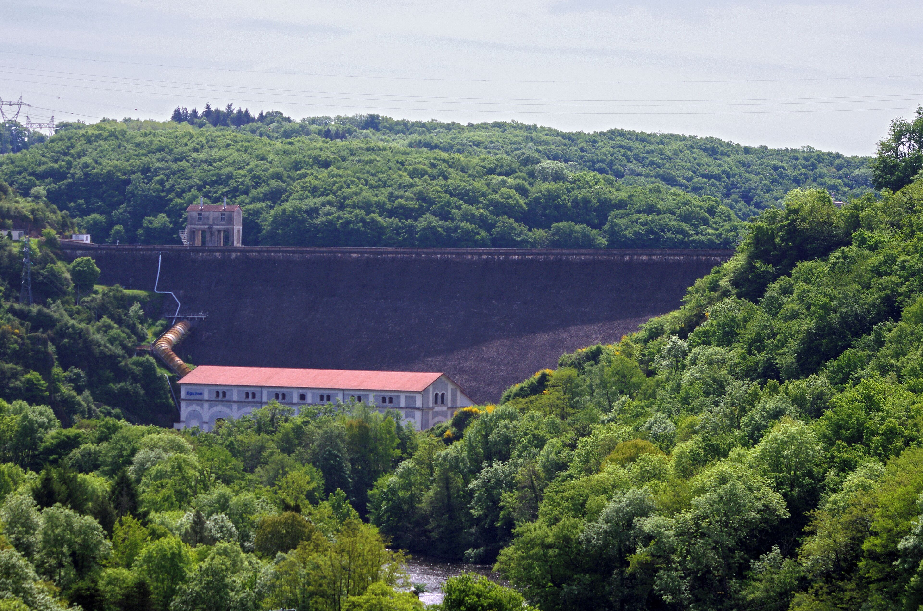 Eguzon-Chantôme (Indre) Le Barrage d'Eguzon, depuis la rive droite.. Barrage hydro-électrique sur la Creuse. L'inauguration du barrage a eu lieu le 5 juin 1926. Journal "Le Midi Socialiste" du dimanche 6 juin 1926: "Une œuvre cyclopéenne Châteauroux, 5 juin. - Ce matin a eu lieu la cérémonie de l'inauguration du barrage et de l'usine d'Eguzon, dans l'Indre. Il s'agissait de déclencher l'usine et de visiter les travaux gigantesques réalisés pour constituer une retenue d'eau, lac artificiel qui mesure environ 18 kilomètres de longueur, 1 kilomètre de large, et contient dans sa vasque environ 54 millions de mètres cubes d'eau apportée par la Creuse. C'est cette eau qui, canalisée, disciplinée, viendra en se libérant actionner les turbines de l'usine et en transformer en énergie électrique transportable à des centaines de kilomètres. Les travaux entrepris en 1921 par Hydro-électrique consistèrent dans la construction d'un barrage de 60 métres de hauteur et d'une usine de 40.000 kilowats de puissance, sur la Creuse. L'équipement de cette chute constitue le premier stade dans I'aménagement de l'énergie du massif central, dont la plus grande partie doit, être utilisés pour l'électrification des chemins de fer et I'alimentation de la région parisienne. Le barrage d'Eguzon est le plus haut barrage de France. Il a entraîné l'emploi de 210.000 mètres cubes de béton. Il est susceptible d'évacuer un débit de 2.000 mètres cubes. L'énergie produite par t'usine sera en annee moyenne, de 120 millions de kilowats-heure." La construction du barrage a nécessité l'apport de main-d'oeuvre étrangère : "D’autres types de chantiers comme celui du barrage d’Eguzon, projet d’électrification d’intérêt national ont nécessité la venue d’une main-d’oeuvre étrangère nombreuse. Ce chantier qui a débuté en 1916 s’est achevé en 1926. La cité créée alors pour loger les ouvriers rassemble jusqu’à 1 500 étrangers soit l'équivalent de la population d’Eguzon même, originaires d’Europe, d’Afrique et d’Asie. (Histoire et mémoire des immigrations en Région Centre - Rapport final mai 2008 - Coordination : Sylvie Aprile, Pierre Billion, Hélène Bertheleu) Le journal "le Dimanche-Illustré du 7 décembre 1930 (N°406) légendait une photo du barrage tout neuf : "Oeuvre de titans : le Barrage d'Eguzon. Le barrage d'Eguzon, dans la Creuse, est un des plus représentatif élément de l'énergie et du génie humain: construit en ciment armé, haut de 60 mètres, large de 55 mètres à sa base, il retient les eaux de la Creuse. " Le journal dévoilait la maquette d'un "train mû par une hélice comme un avion", oeuvre d'un ingénieur suisse qui espérait aini atteindre 300 km. à l'heure. L'appareil de TSF "radiociné" coûtait 1540 francs, mais il était possible de l'acheter pout 160 francs, et le reste en 12 mensualités de 110 francs. Garantie 1 an. On pouvait se procurer l'appareil dans la succursale "radiociné" de Blois, 20 rue du commerce. La "Nouvelle République" du 20 octobre 2014 pose la question de la rupture du barrage. "Dans l'éventualité où le barrage d'Éguzon venait à rompre, un système d'alerte vient d'être mis en place pour assurer la sécurité de la population des 21 communes qui pourraient risquer " une inondation à cinétique rapide ". Des sirènes spécifiques ont été installées."